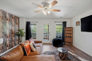 A living room with a brown leather sofa, a ceiling fan, a glass coffee table, and a wooden bookshelf. - Private Pool & Patio & Poker & Kids Play Room (San Antonio)