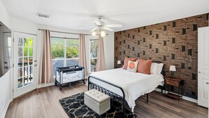 A bedroom with a bed, a ceiling fan, a wall with a geometric pattern, a window with curtains, and a door. - Private Pool & Patio & Poker & Kids Play Room (San Antonio)
