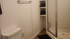 Un baño con inodoro, cabina de ducha y estante.