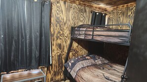 Una cama litera con un edredón estampado, un aparador de madera y cortinas.