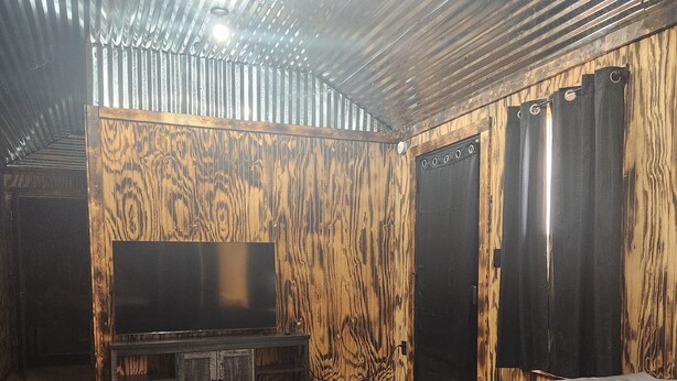 Una habitación con pared de madera, un sofá negro, un televisor y una alfombra negra.