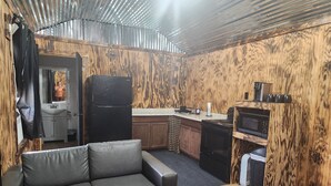 Cocina compacta equipada con refrigerador, microondas y estufa. Se observa un muro de madera y un sofá de cuero negro.