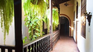 A corridor with a railing, hanging plants, and a tiled floor. - Casa Estrella (Cartagena)