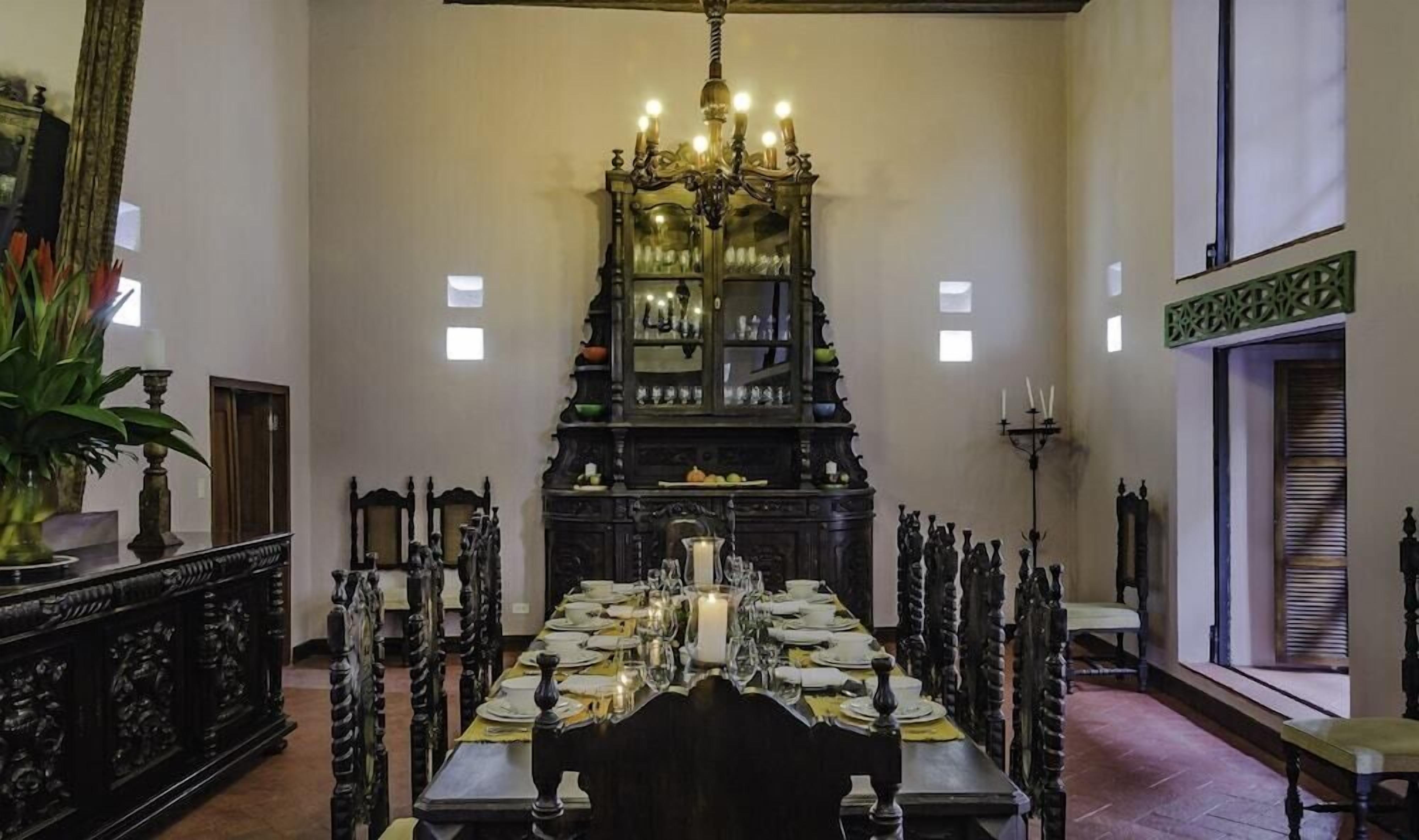 Une salle à manger avec une longue table dressée pour le repas, un lustre et un buffet contenant de la verrerie.