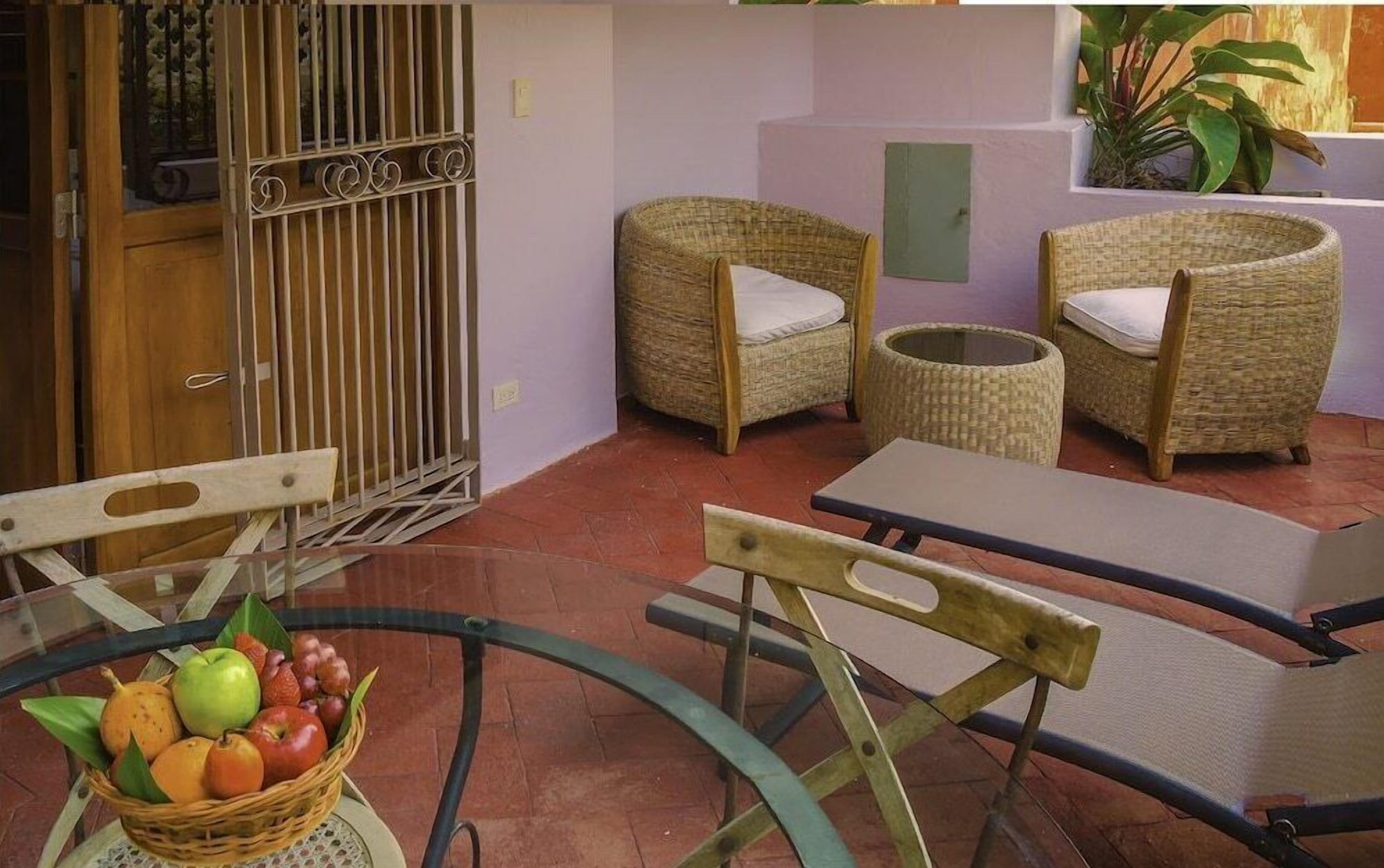 A room with wicker furniture, a glass table with fruit, and a metal gate.