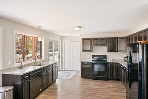 A modern kitchen with dark cabinets, a stainless steel refrigerator, and a large window.