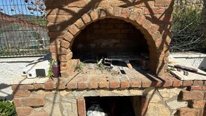 Een buitenoven van baksteen met schoorsteen, omringd door een metalen hek.