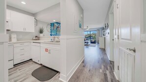 A modern kitchen with white cabinetry, a dining area with a blue sofa, and a view to a balcony. - Fairway to Shore - your peaceful, fun and cozy beach villa! (Panama City Beach)