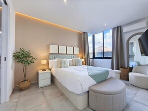 Ein modernes Hotelzimmer mit einem großen Bett, Nachttischen, einer Topfpflanze und Blick auf die Berge.