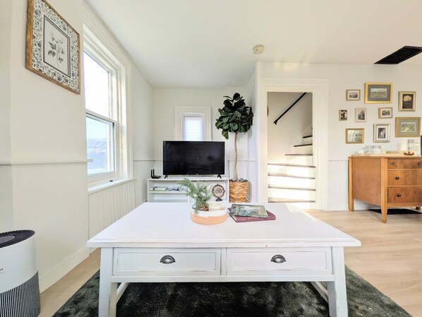 A room with a white table, a TV, a plant, and a staircase. - Checkerboard guest house close to charming downtown + family-friendly yard space (Cobourg)