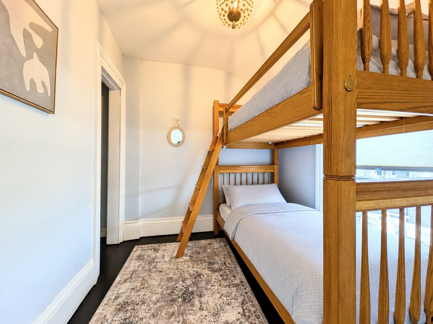 Een slaapkamer met een stapelbed, een tapijtel met dessin, een ronde spiegel en een lijst met een afbeelding aan de muur.