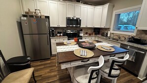 Una cocina moderna con armarios blancos, electrodomésticos de acero inoxidable, una mesa de comedor con individuales y una ventana con persianas.
