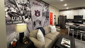 Una sala de estar con un sofá, mesa de centro, lámpara y una pared decorada con recuerdos del equipo Auburn de fútbol.