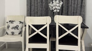 A dining area with a table, two chairs, a bench, a painting, and a vase of flowers. - Greg black apartment - WITH AC/NETFLIX,HOTSHOWER (Mombasa)