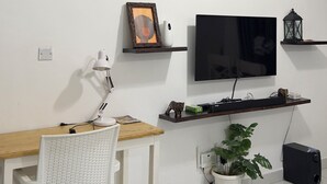 A modern living room with a flat-screen TV, a wooden dining table, a white chair, a small potted plant, and a black speaker. - Greg black apartment - WITH AC/NETFLIX,HOTSHOWER (Mombasa)