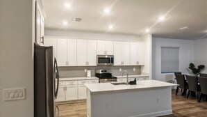 Een moderne keuken met witte kastjes, een roestvrijstalen koelkast, een magnetron en een groot keukenblok met een spoelbak.