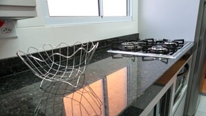 Eine Küche mit einem Gasherd, einem Metallregal und einem Fenster über der Arbeitsplatte.
