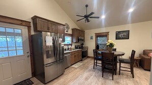 A kitchen with wooden cabinets, a stainless steel refrigerator, a ceiling fan, and a dining area with chairs and a table. - Little Brick House - 10min from New River Gorge Bridge (Fayetteville)