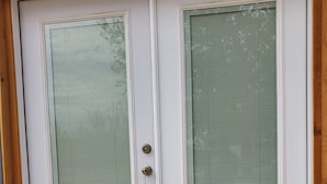 Puerta doble blanca con un panel de vidrio y un ojo de cerradura, enmarcada en madera.