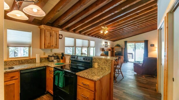 Une cuisine dotée de meubles en bois, de plans de travail en granit, d’une cuisinière noire et d’un plafond avec des poutres apparentes.