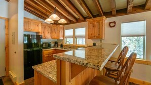 Une cuisine avec des meubles en bois, des plans de travail en granit, un réfrigérateur noir et un luminaire suspendu.