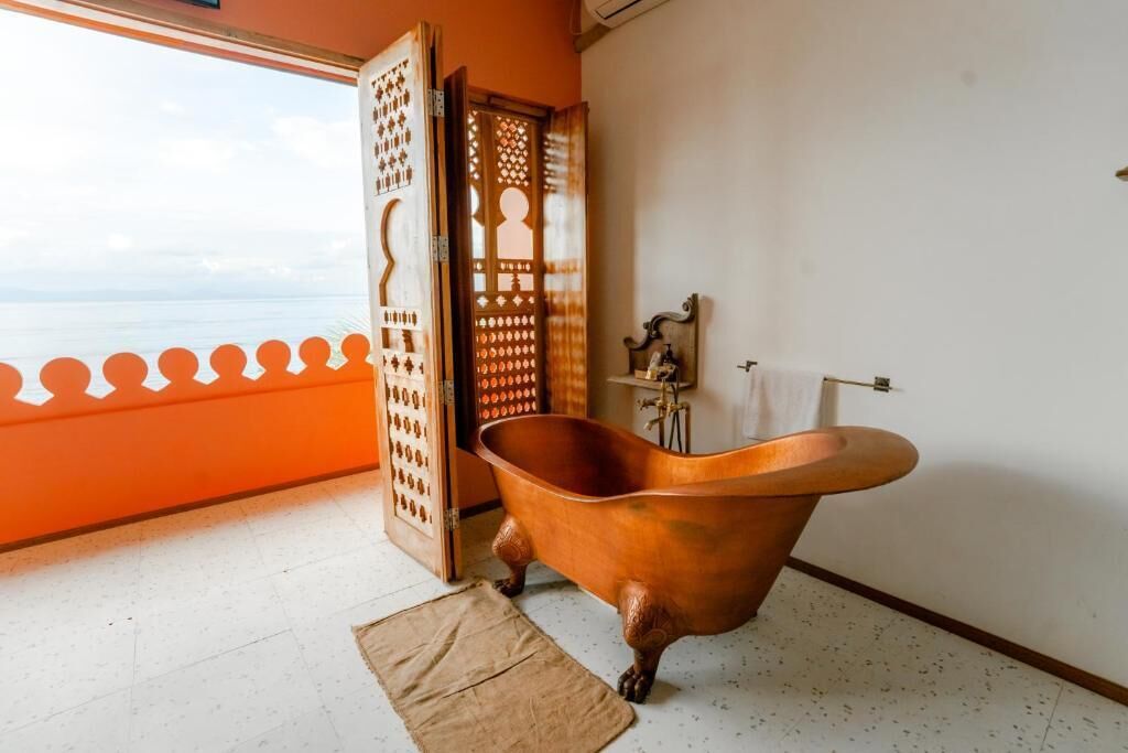 A room with a large bathtub, a wooden partition, and a view of the sea.