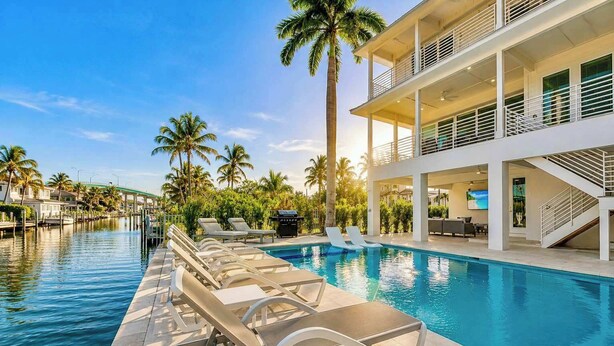 A modern hotel with a pool, lounge chairs, and a view of the waterway. - Salt House · 2026 Luxury · 6 King Suites 2 Masters (Fort Myers Beach)