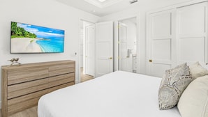 A bedroom with a bed, a wooden dresser, a TV on the wall, and white doors. - Salt House · 2026 Luxury · 6 King Suites 2 Masters (Fort Myers Beach)