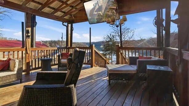 Een houten terras met rieten meubilair, een aan het plafond bevestigde televisie en uitzicht op een berglandschap.