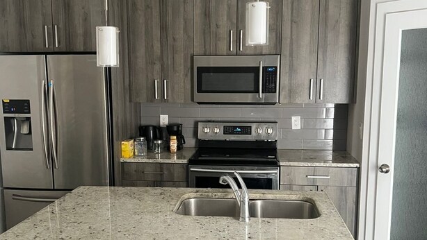 Cozinha moderna com bancadas de granito, eletrodomésticos de aço inoxidável e armários de madeira escura.