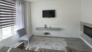 Uma sala de estar moderna com televisão de tela plana fixada em uma parede com padrão de tijolos, um sofá, uma mesa pequena e uma lareira.