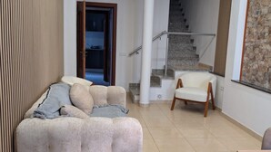 Un salon moderne avec un canapé, un fauteuil, un escalier et un mur en pierre.