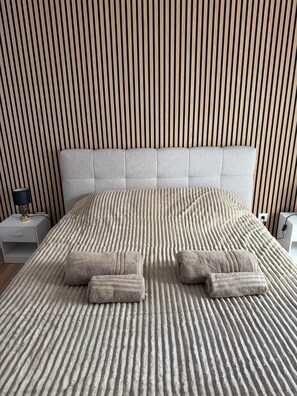 Cama bem arrumada com colcha listrada e duas toalhas dobradas.