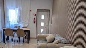 Une pièce comprenant un lit, un canapé, une table à manger avec des chaises, un extincteur et une fenêtre avec des rideaux.