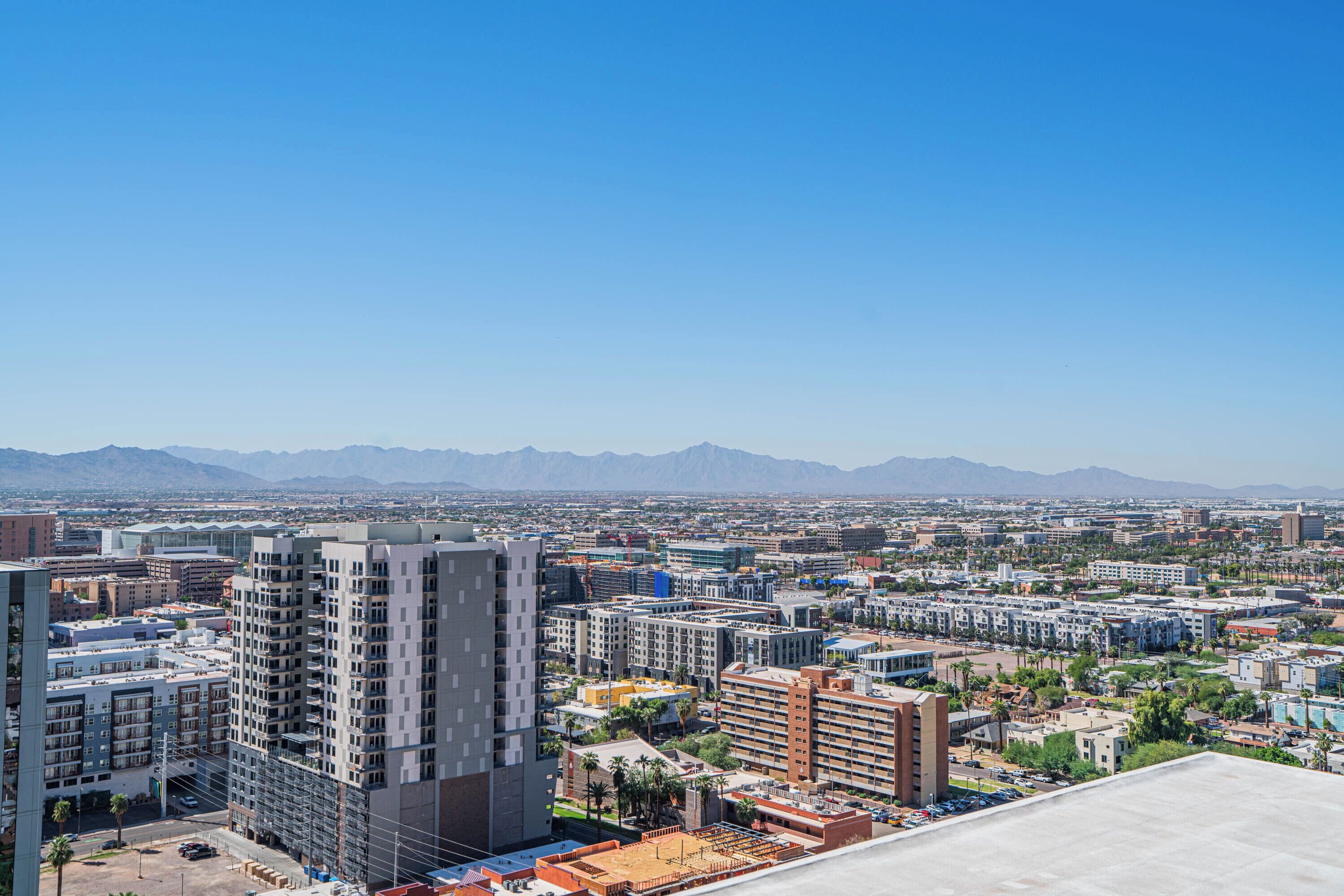 A cityscape with high-rise buildings, a clear sky, and distant mountains.