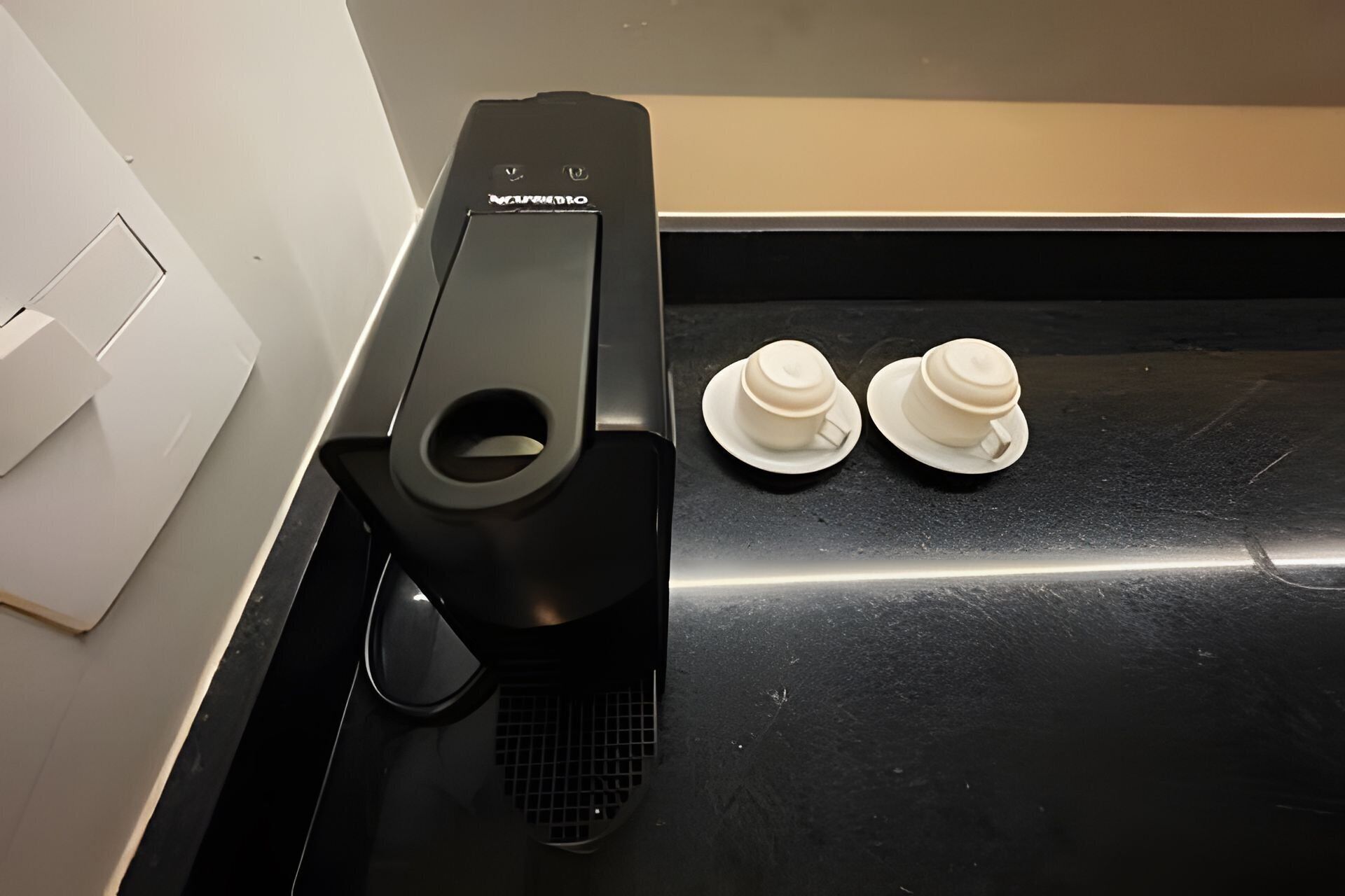 Una máquina de café y dos tazas blancas sobre una encimera negra.