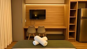 Ein Hotelzimmer mit Bett, Wandfernseher, zwei Stühlen, einem Kühlschrank und Holzvertäfelung.