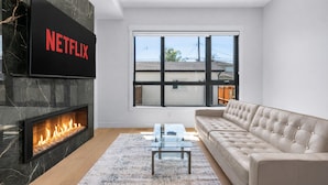 Un salon moderne doté d’une cheminée, d’une grande fenêtre, d’un canapé et d’un téléviseur à écran plat affichant le logo « NETFLIX ».
