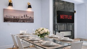 Un coin repas avec une table en verre, des chaises blanches et un tableau représentant un paysage urbain.
