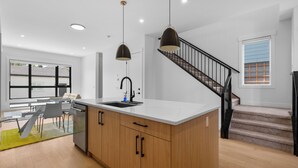 Une cuisine moderne dotée d’un îlot central, d’un coin repas avec une table et des chaises, et d’un escalier menant à l’étage supérieur.