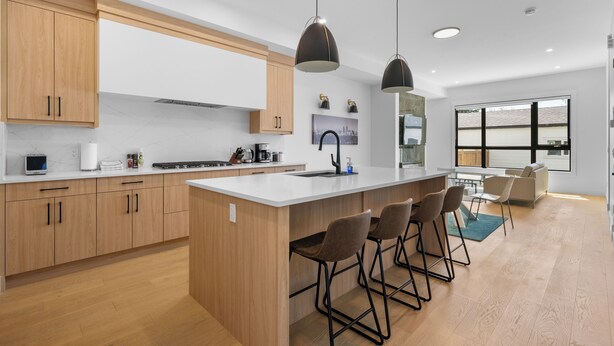 Une cuisine moderne avec des meubles en bois, un grand îlot central, des tabourets de bar et des luminaires suspendus.