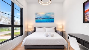 Une chambre d’hôtel moderne avec un grand lit, deux tables de chevet, un bureau et un tableau au-dessus du lit.