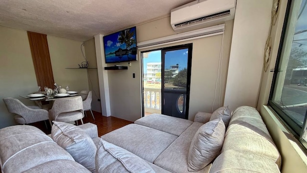 A living area with a sofa, a dining table with chairs, a TV, and a balcony with a view. - ALMAR (Puerto Baquerizo Moreno)