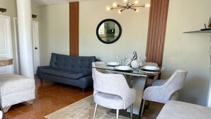 A dining area with a glass table, grey upholstered chairs, and a modern chandelier. - ALMAR (Puerto Baquerizo Moreno)