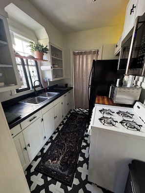 Una cocina con piso de diseño blanco y negro, estufa, pileta, alacenas y una planta en maceta.