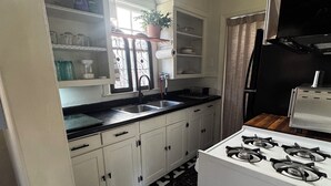 Een keuken met witte kasten, een zwart-wit vloerkleed, een gasfornuis en een raam met een plant.