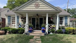 A two-story house with a porch, a front door, and a small garden area with potted plants. - ROBYN’S NEST🪺 🪺 
2 bedroom in the heart of beautiful historic Central Gardens. (Memphis)