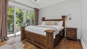 Een slaapkamer met een houten bed, nachtkastje, plafondventilator en uitzicht door grote ramen.