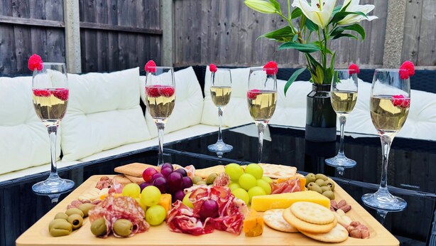 Ett träbord med en bricka med charkuterier, glas med vitt vin och en krukväxt.