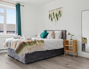 Ein Schlafzimmer mit einem Bett, einem Nachttisch, einer Wanddekoration aus Makramee und einem Fenster mit Vorhängen.
